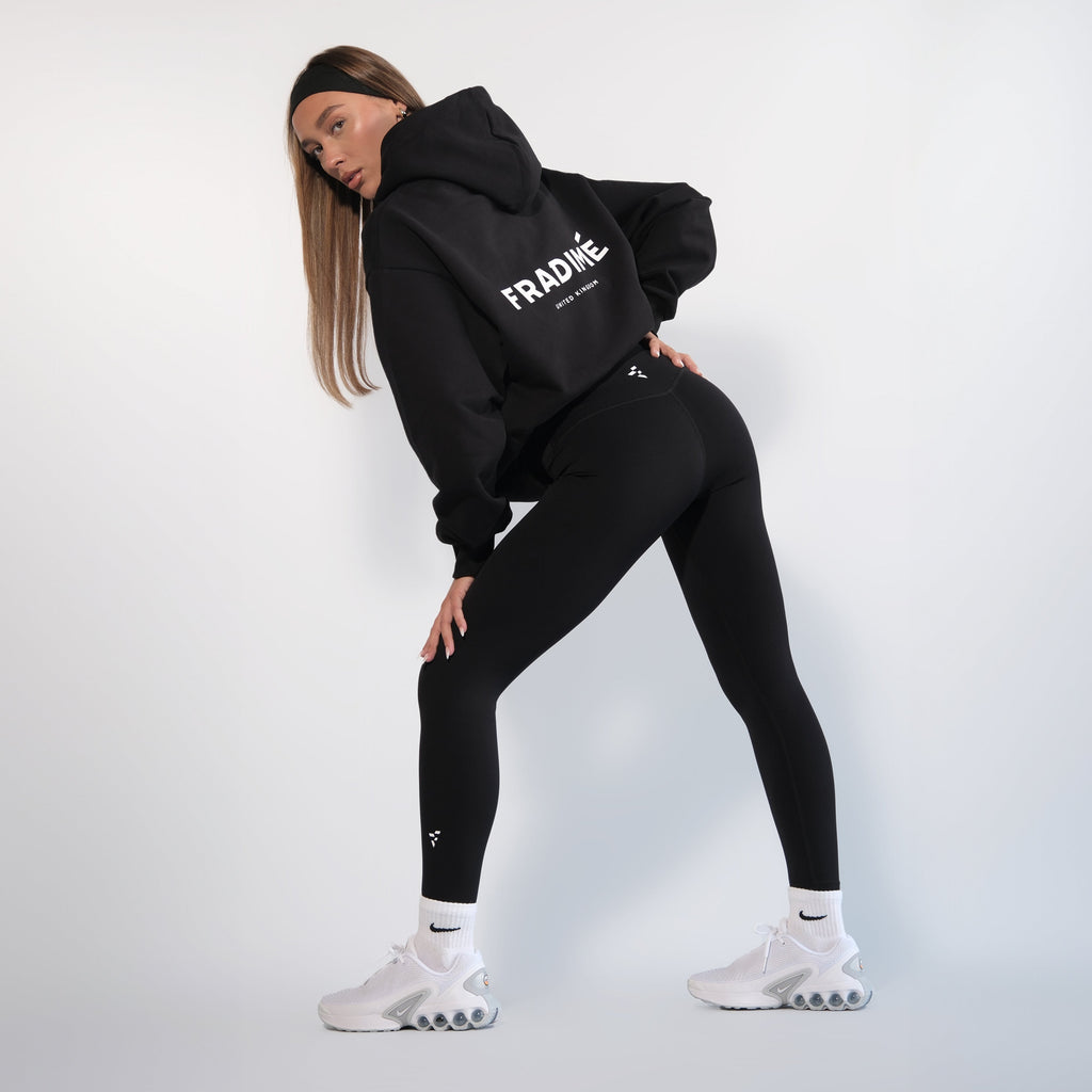 Person wearing a black hoodie and leggings with 'Fradimé' branding on a white background