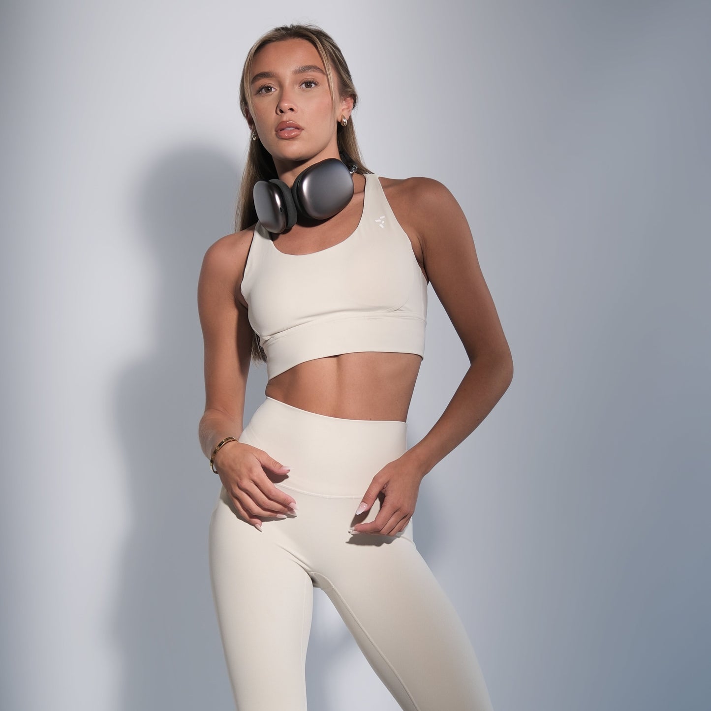 Woman wearing a white sports bra and leggings set with headphones on a gray background