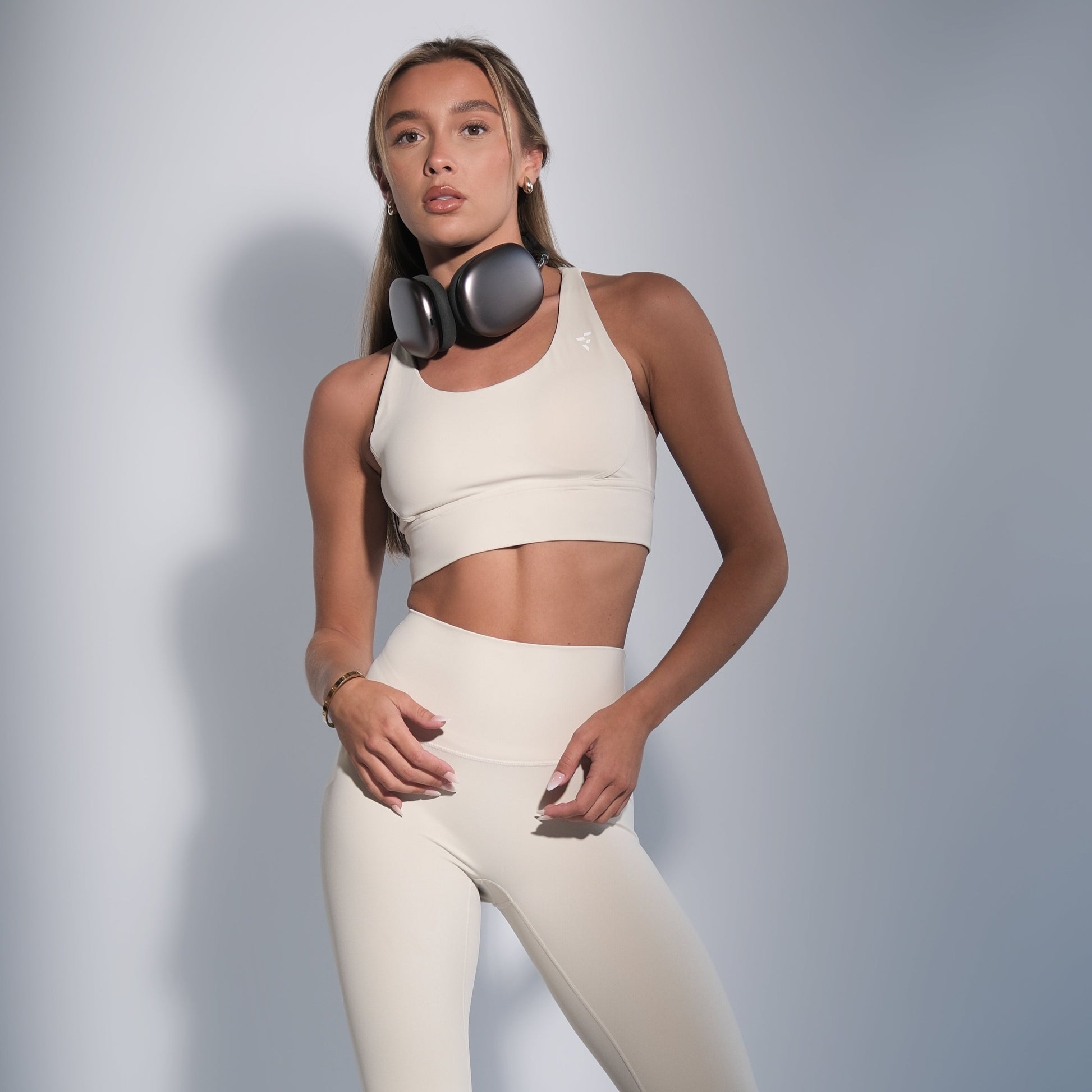 Woman wearing a white sports bra and leggings set with headphones on a gray background